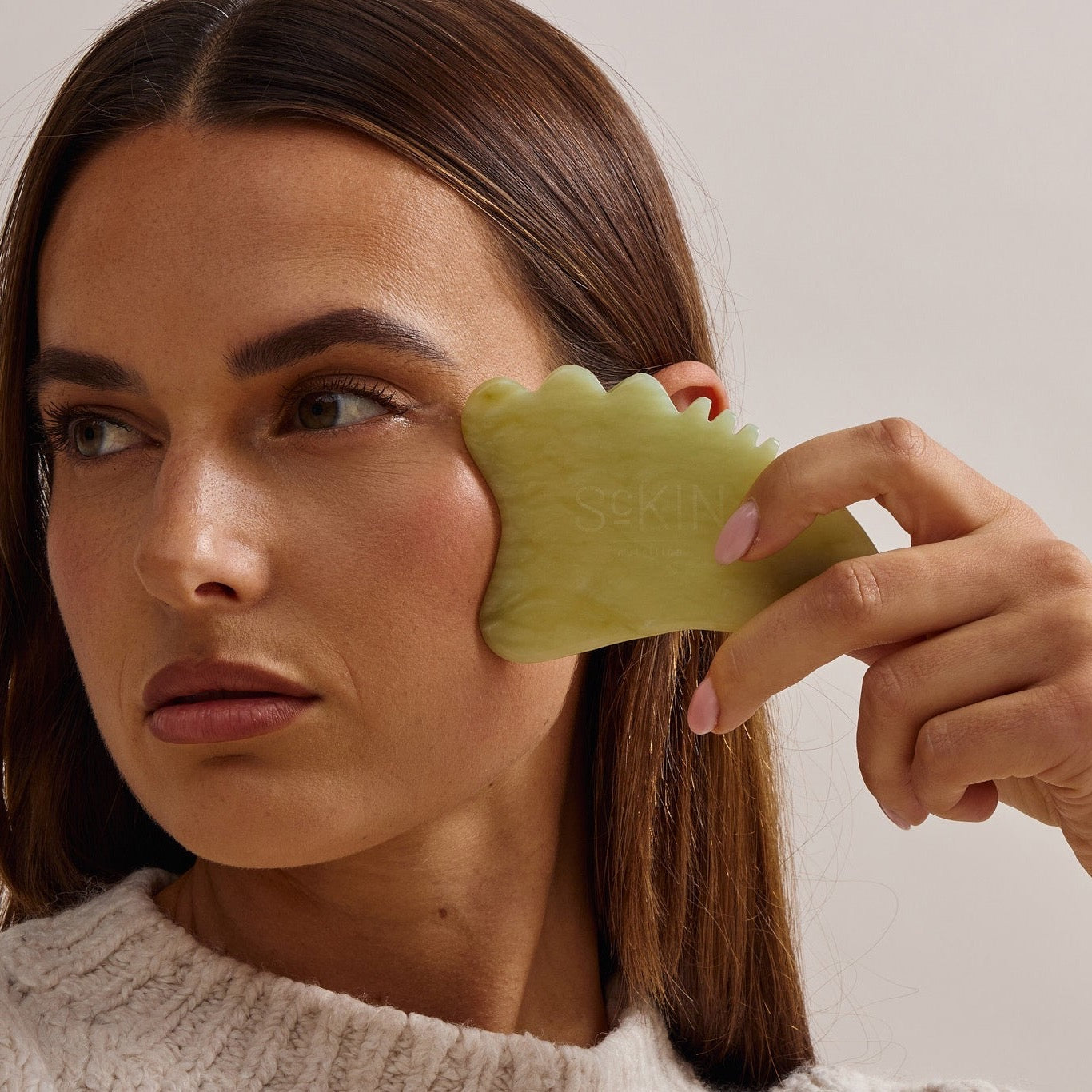 Vrouw masseert haar wang met een jade gua sha